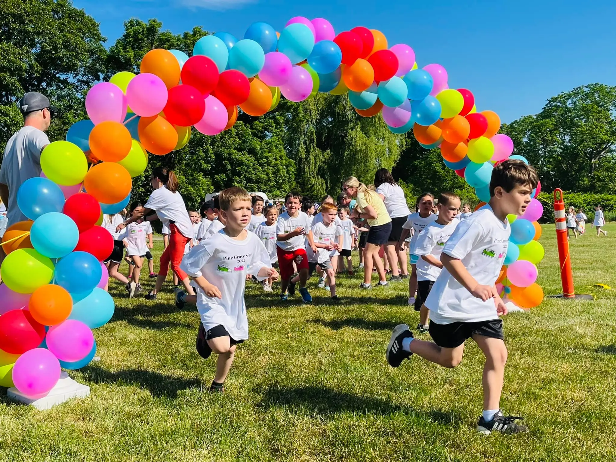 Kids running through balloon arch on grassy field