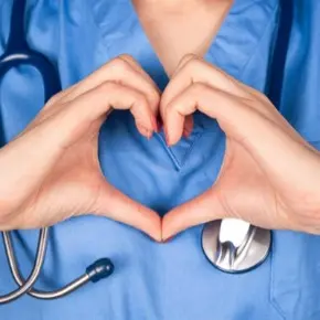 Nurse in blue scrubs with a stethoscope making a heart shape with her hands