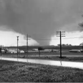 Black and white photo of a tornado with buildings and power lines in front