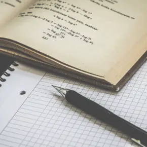 Math textbook open on top of graph paper with a mechanical pencil also on the paper