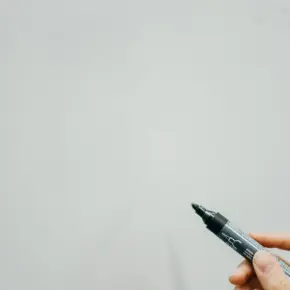 A marker held paused over the surface of a whiteboard