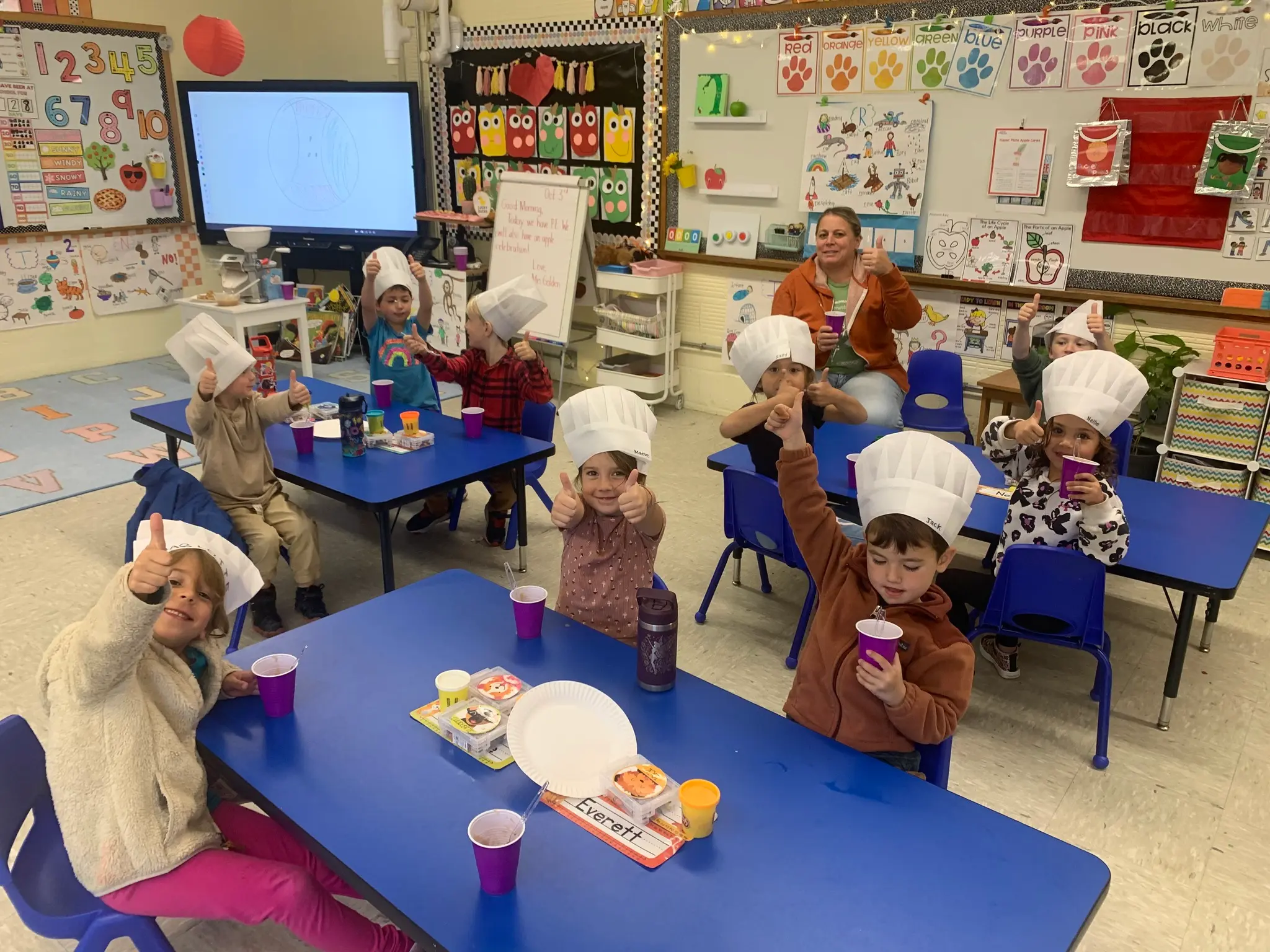 students sitting at tables giving a thumbs up wearing chefs hats
